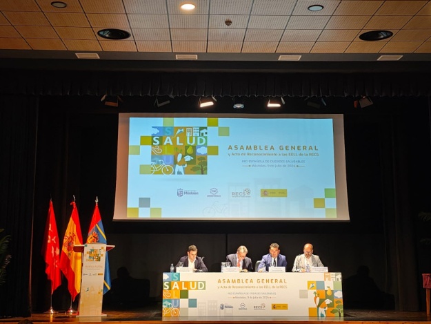 Mesa de ponentes y pantalla en una de las intervenciones de la asamblea general de la Xarxa Estatal de Ciutats Saludables
