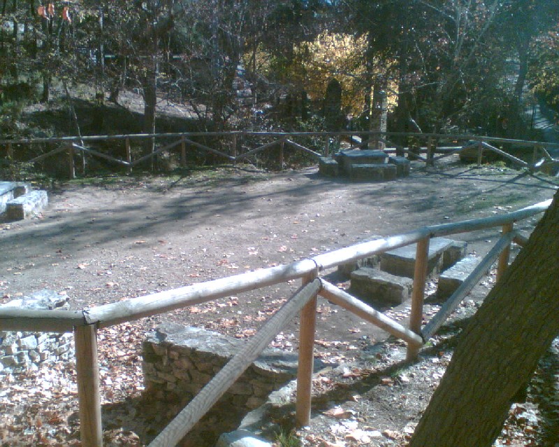 Mesas rectangulares y bancos de piedra en zona delimitada por una valla de madera