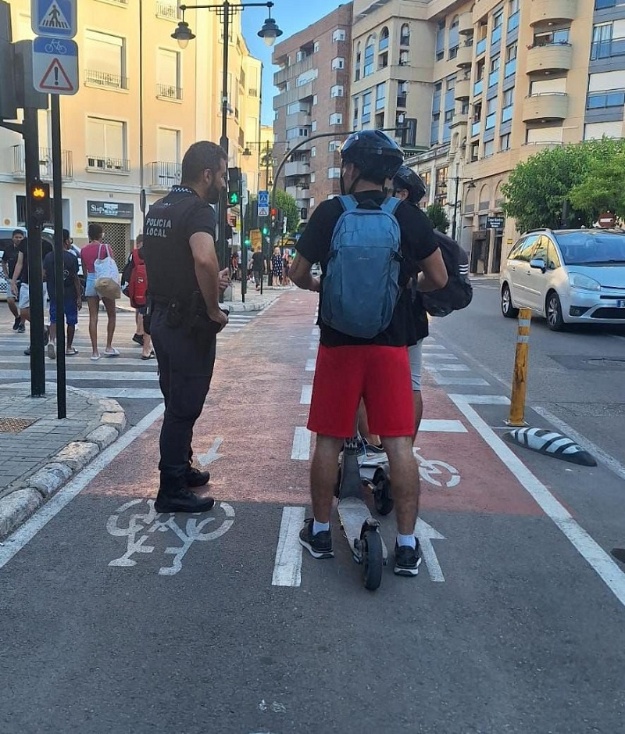 Un policia local i dos usuaris de vehicles de mobilitat personal en el carril bici del carrer dels Alçamora