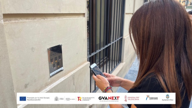 Foto de una joven interactuando con el móvil en una de las placas situada en la calle de Sant Llorenç