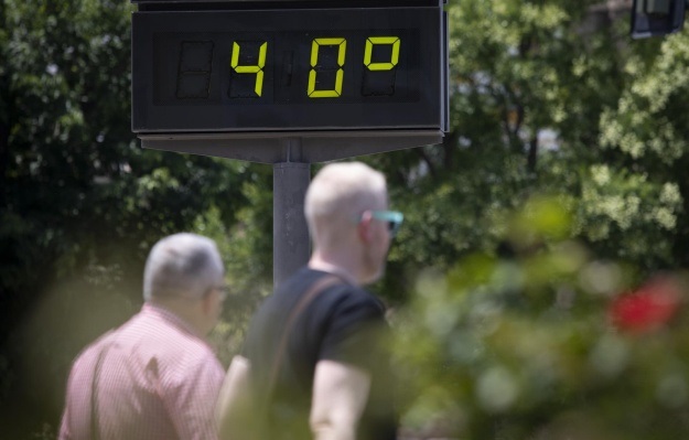 Foto de dos peatones pasando cerca de un indicador urbano de temperatura que marca 40 grados
