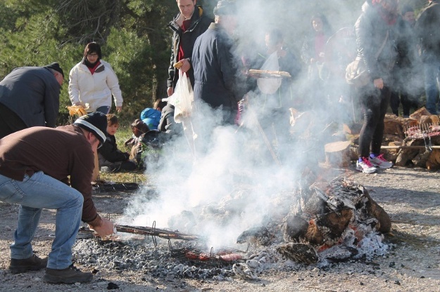Grupo de romeros y romeras en una hoguera asando embutido y carne