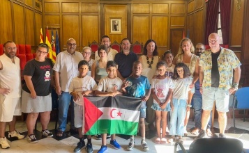 El alcalde, el vicealcalde y la concejala de Infancia posan en el Salón de Plenos con los 5 menores y las familias de acogida con la bandera saharaui