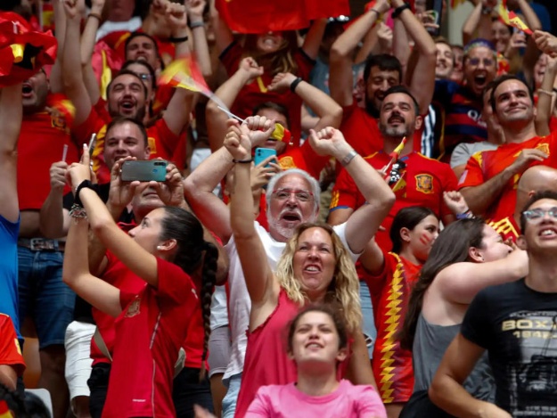 Aficionados de la selección española de fútbol en pie, vitoreando en el campo