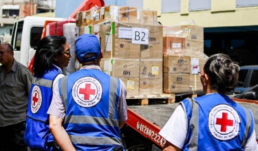 Cooperantes de la Cruz Roja observando un camión cargado de cajas de donaciones