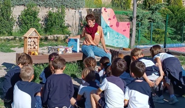 Xiquets i xiquetes al parc, asseguts en la gespa, escoltant l'educadora