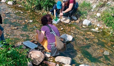 Dos adults i un xiquet examinen una mostra d'aigua del riu sobre una safata durant una activitat ambiental