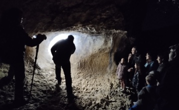 El guia il·lumina una paret amb pintures rupestres en la visita nocturna a La Sarga davant l'atenta mirada del públic assistent
