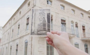 captura de pantalla del vídeo sobre el modernisme en el qual es veu una mà sostenint una foto antiga amb la Casa Escaló de fons