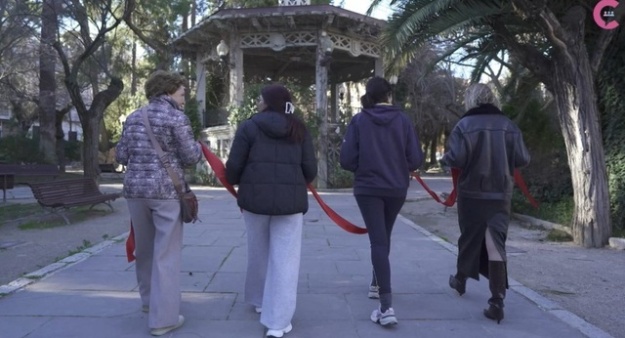 Captura del vídeo del Consell Social en el qual es veu a quatre dones d'esquena sostenint una cinta roja